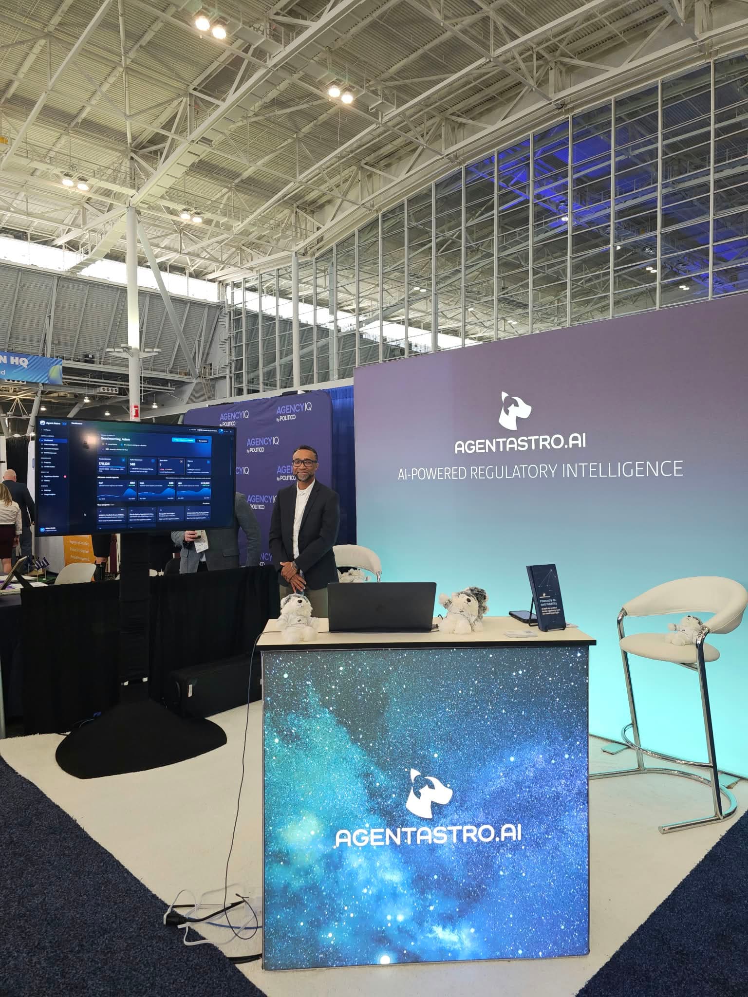 A member of the Agent Astro team at the booth, beside a screen showing the Agent Astro dashboard.
